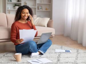 Mulher sorridente trabalhando com laptop e documentos impressos em gráfica rápida.